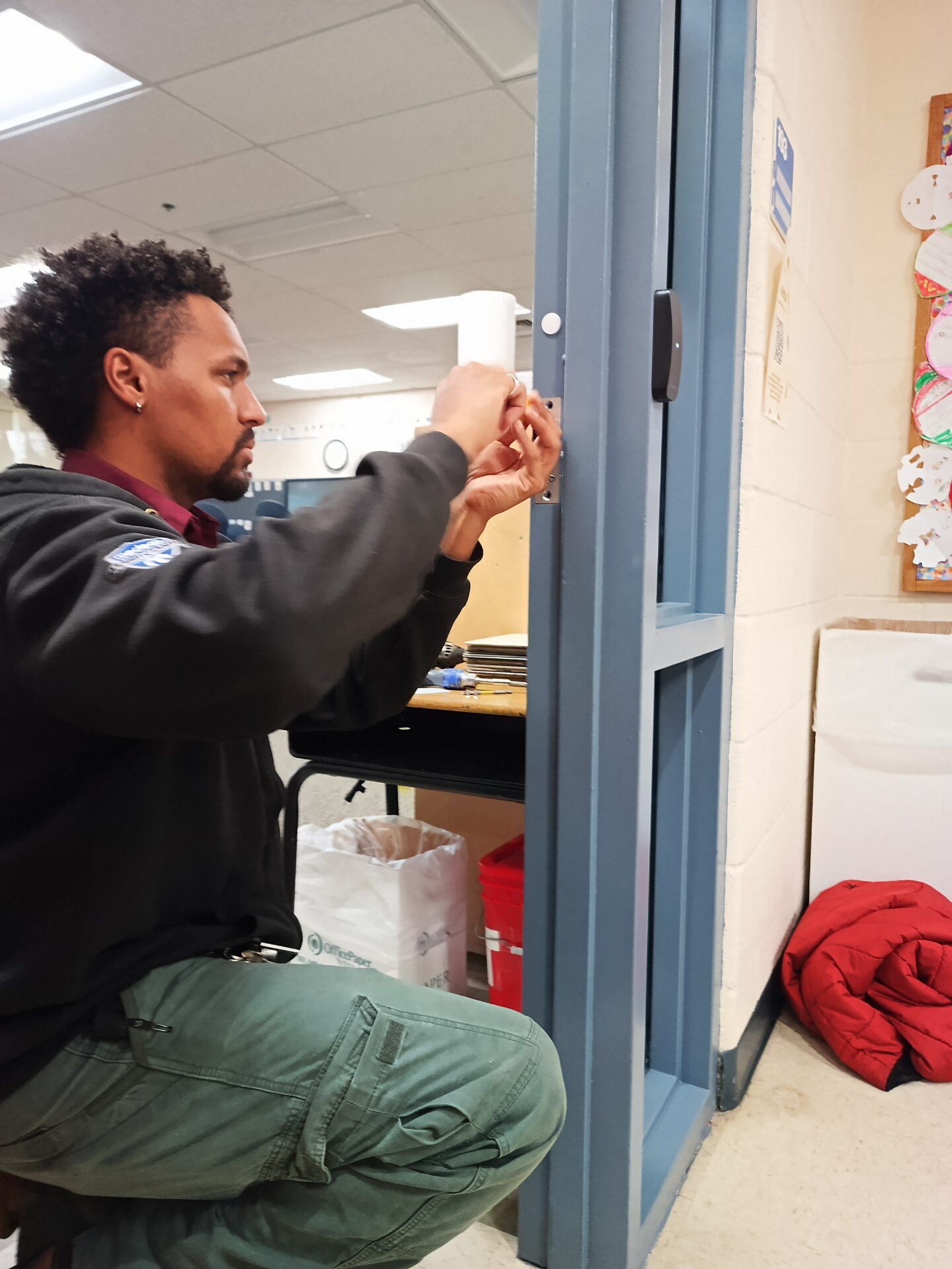 A Security Professional from Able Locksmiths, LLC works on door hardware in a school.