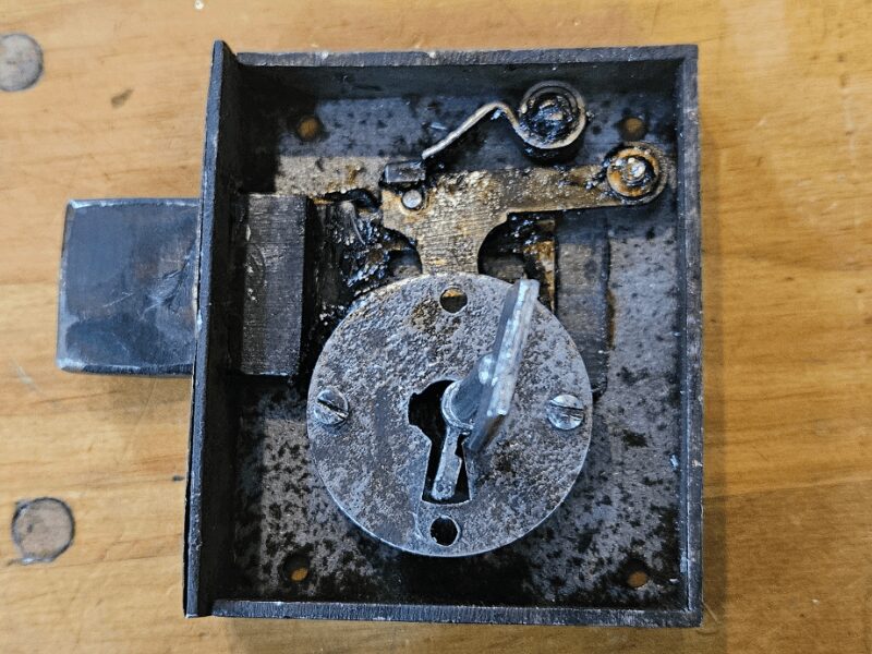 An antique lock sits open showing the internals with a key in the keyhole. 